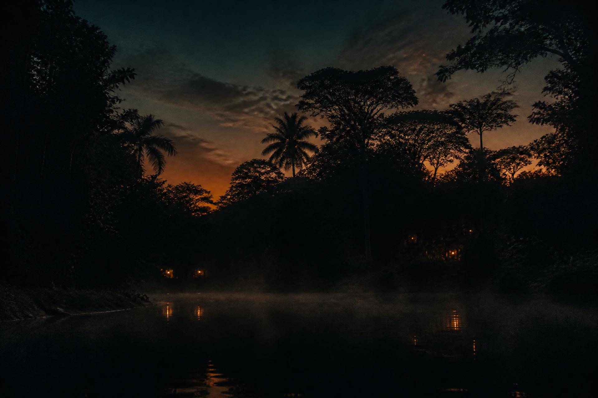 Jungle waterfall and cave opening at dusk, warm light on dark water